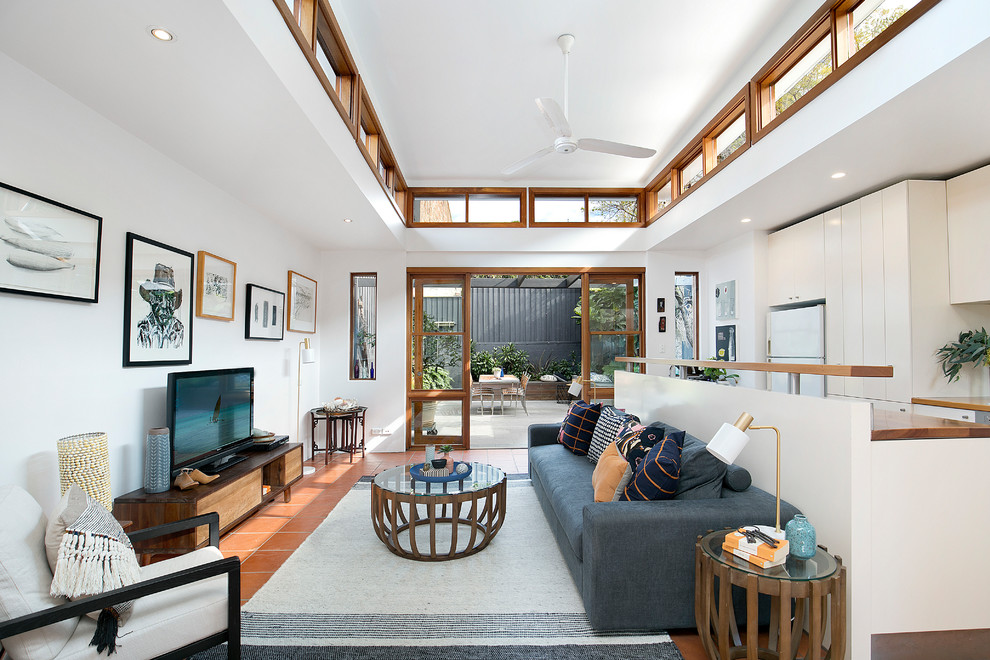 This is an example of a mid-sized transitional open concept living room in Sydney with white walls, terra-cotta floors, no fireplace, a freestanding tv and red floor.