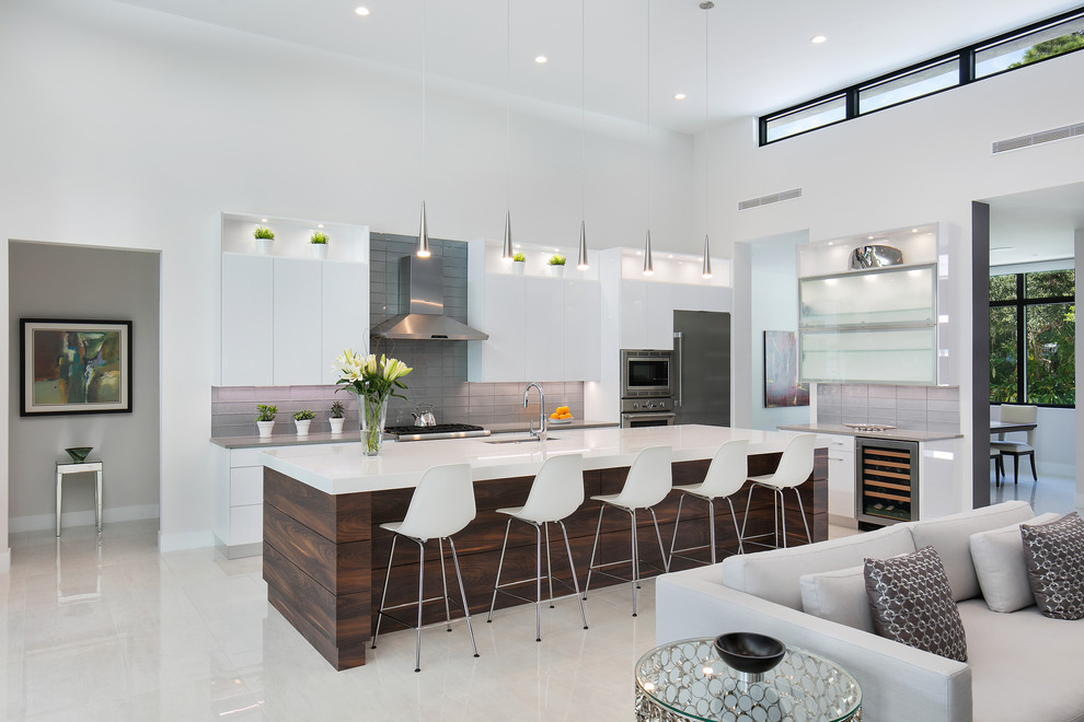 Photo of a large modern l-shaped open plan kitchen in Tampa with an undermount sink, flat-panel cabinets, white cabinets, quartz benchtops, grey splashback, glass tile splashback, stainless steel appliances, porcelain floors, with island, white floor and grey benchtop.