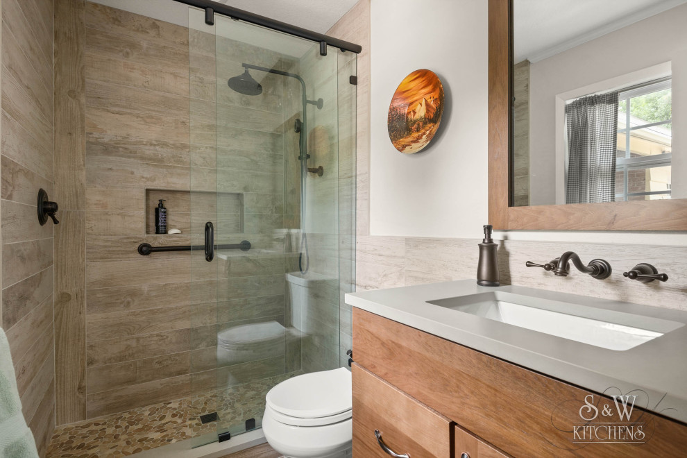 Photo of a mid-sized master bathroom in Orlando with louvered cabinets, medium wood cabinets, a two-piece toilet, brown tile, wood-look tile, grey walls, wood-look tile, an undermount sink, engineered quartz benchtops, brown floor, a sliding shower screen, grey benchtops, a niche and a single vanity.