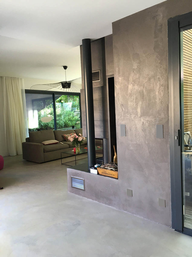 Mittelgroßes, Offenes Modernes Wohnzimmer mit grauer Wandfarbe, Betonboden, Eckkamin, Kaminumrandung aus Beton und TV-Wand in Sonstige