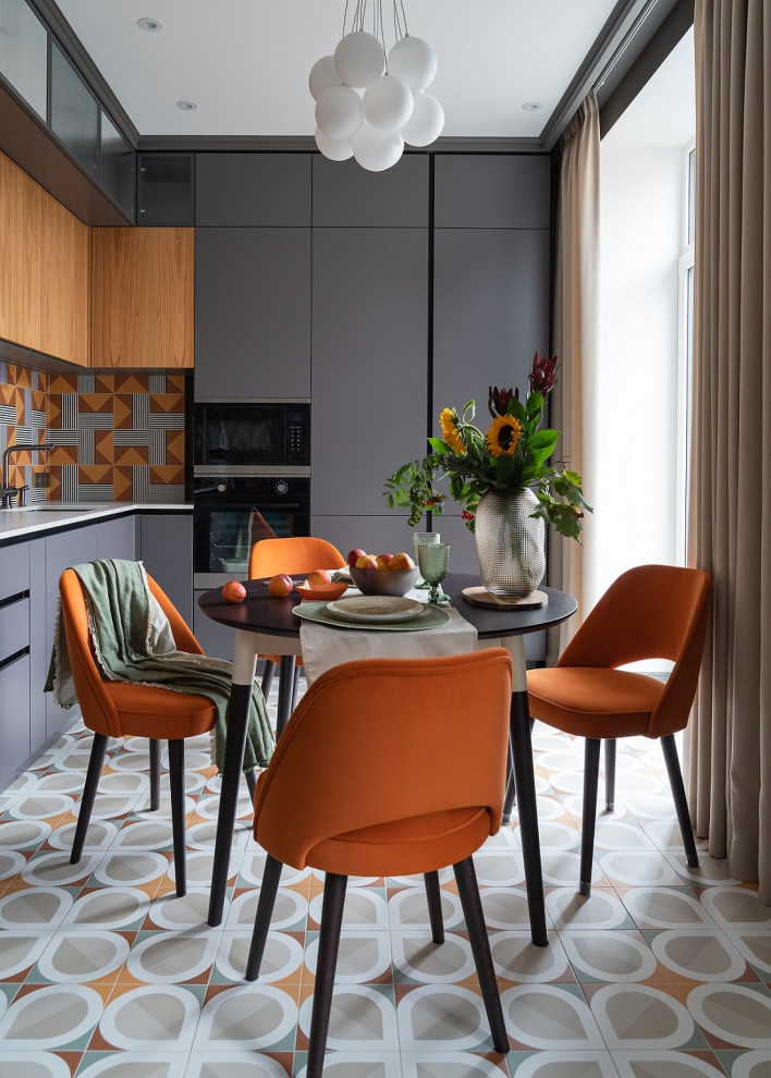 Пример оригинального дизайна: серо-белая кухня в современном стиле с серыми фасадами, столешницей из кварцевого агломерата, оранжевым фартуком, техникой из нержавеющей стали, полом из керамогранита и белой столешницей