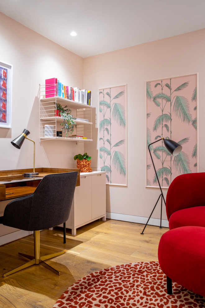 Mid-sized contemporary study room in London with pink walls, light hardwood floors, a freestanding desk and wallpaper.