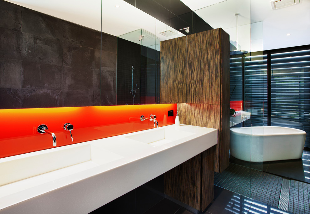 Inspiration for a contemporary bathroom in Melbourne with a freestanding tub, a curbless shower, orange tile, glass sheet wall, flat-panel cabinets, dark wood cabinets, a bidet, black walls, porcelain floors, an integrated sink, black floor and an open shower.