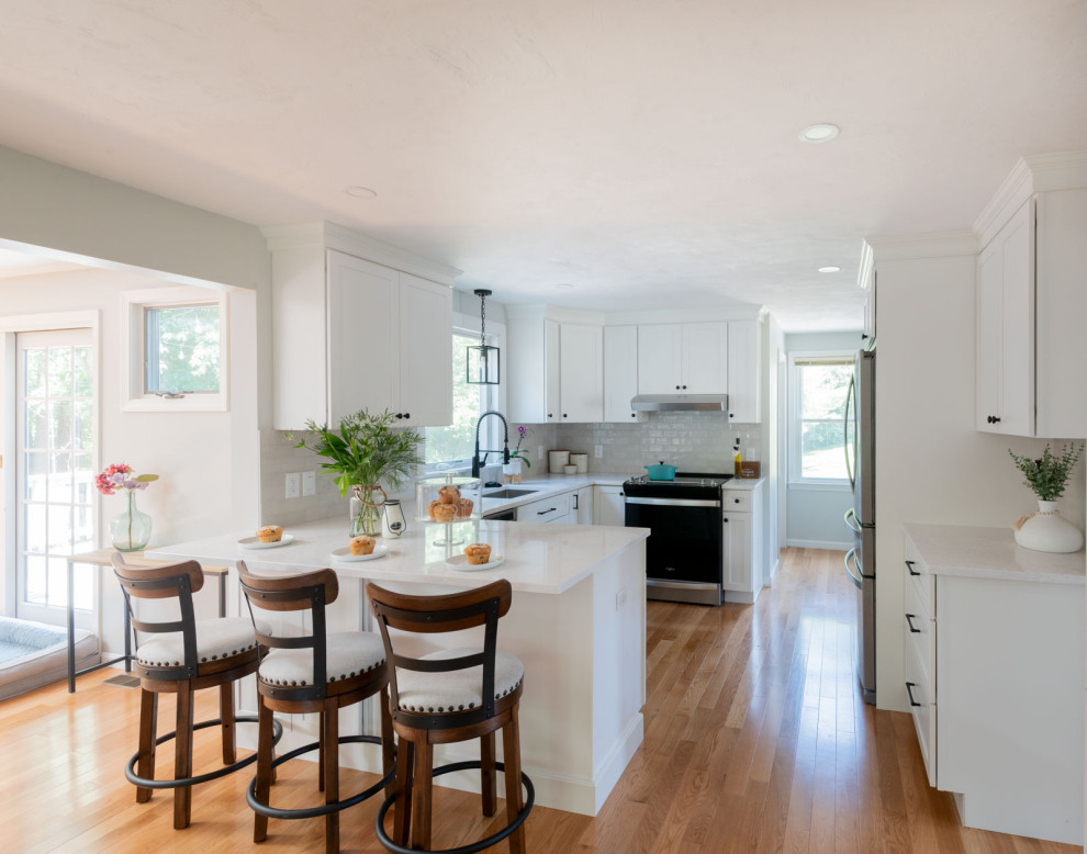Mid-sized transitional u-shaped medium tone wood floor and brown floor enclosed kitchen photo in Boston with an undermount sink, shaker cabinets, white cabinets, quartz countertops, white backsplash, subway tile backsplash, stainless steel appliances, a peninsula and white countertops