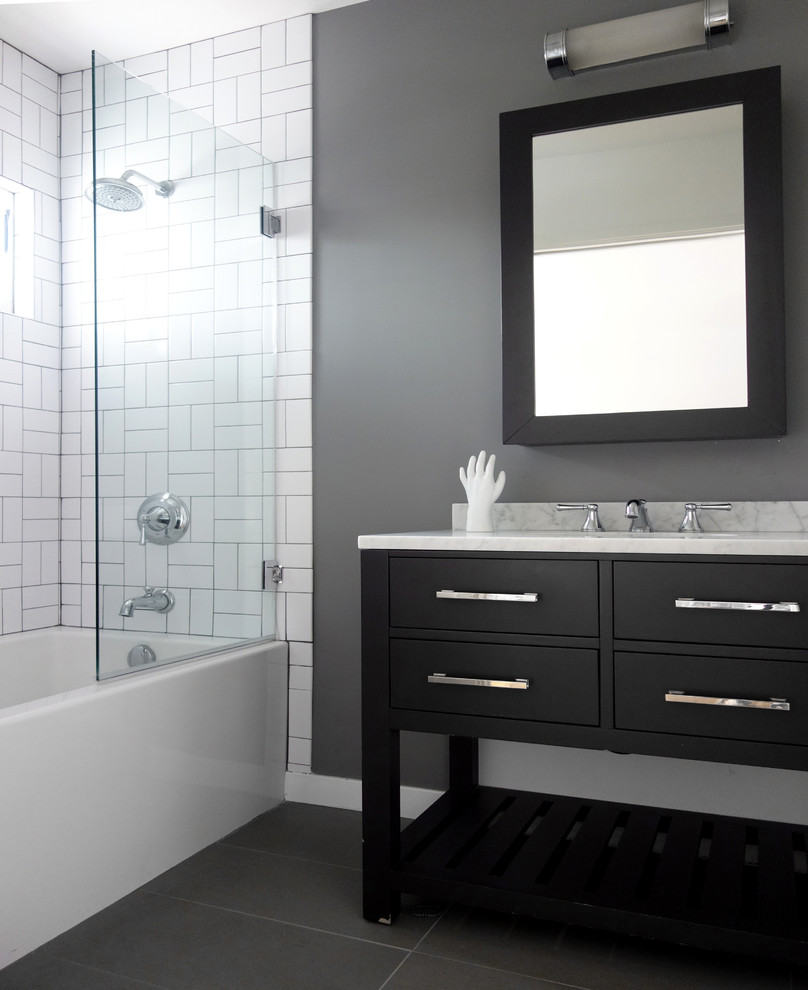 This is an example of a mid-sized contemporary bathroom in Los Angeles with an undermount sink, furniture-like cabinets, grey cabinets, marble benchtops, a drop-in tub, a shower/bathtub combo, a two-piece toilet, white tile and porcelain tile.