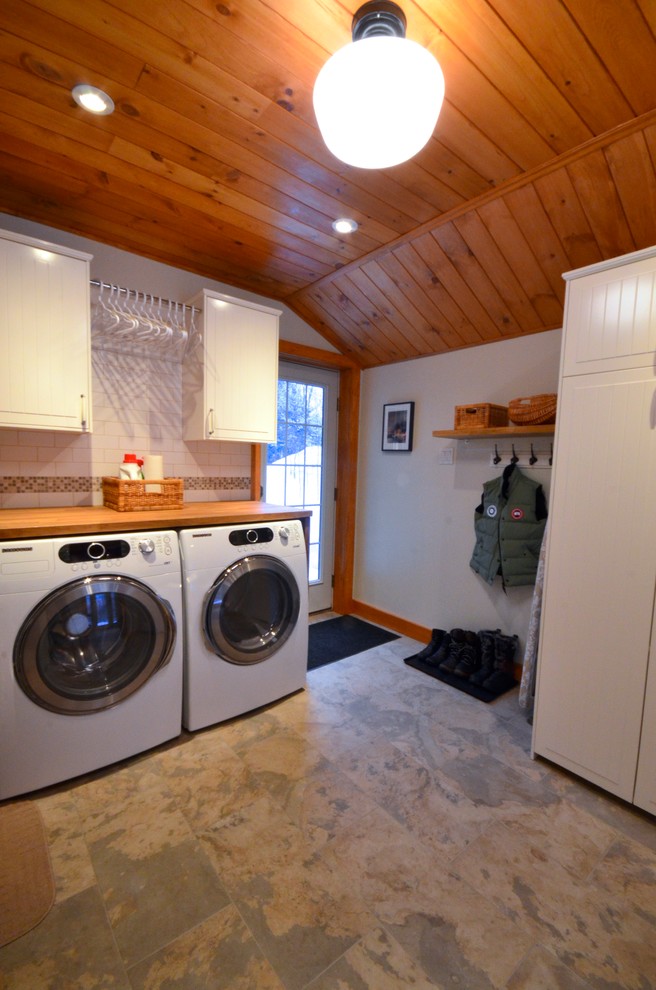 This is an example of a mid-sized transitional single-wall utility room in Ottawa with shaker cabinets, white cabinets, wood benchtops, white walls, slate floors and a side-by-side washer and dryer.