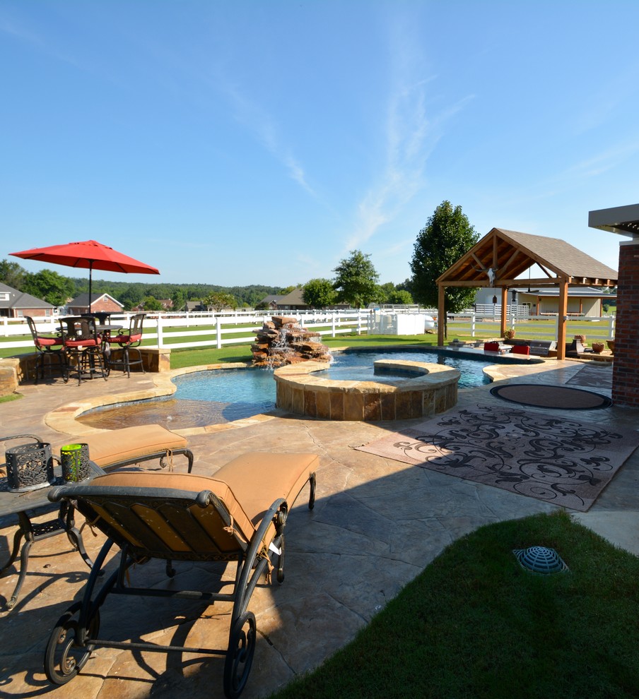 Large country backyard custom-shaped lap pool in Little Rock with a hot tub and stamped concrete.