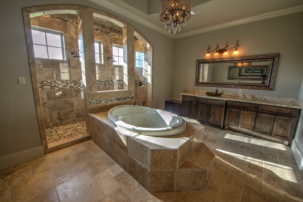 Expansive mediterranean master bathroom in Houston with shaker cabinets, brown cabinets, a drop-in tub, a double shower, a one-piece toilet, beige tile, travertine, beige walls, travertine floors, a vessel sink and granite benchtops.