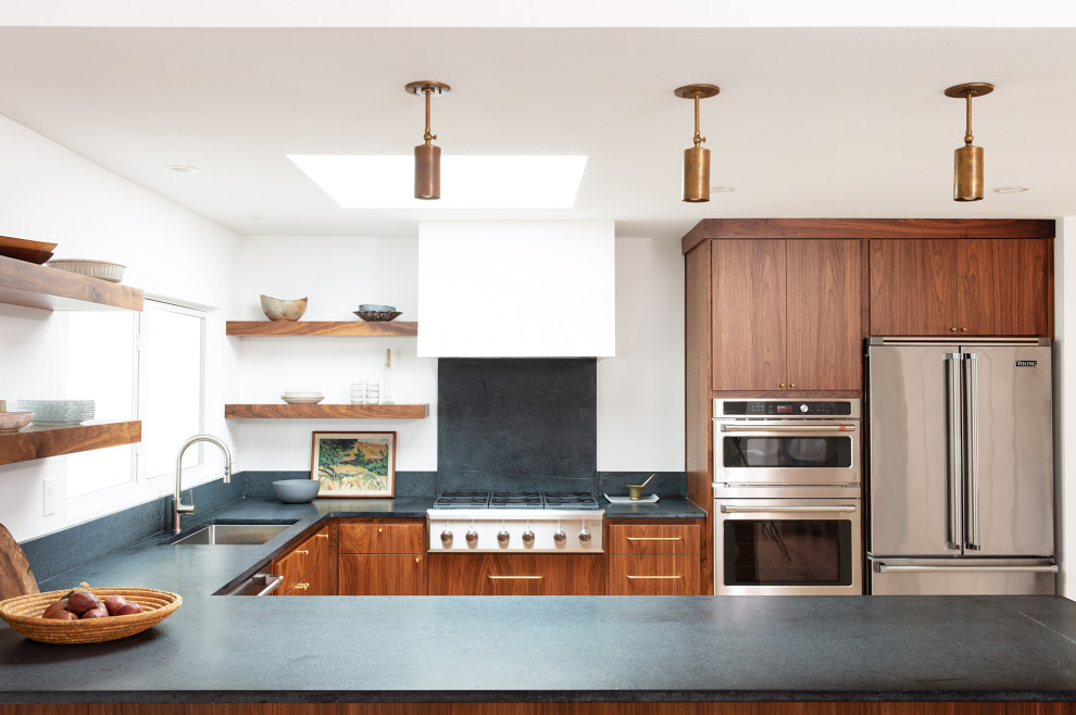 Photo of a retro u-shaped kitchen/diner in Sacramento with a single-bowl sink, flat-panel cabinets, soapstone worktops, stainless steel appliances, light hardwood flooring and a breakfast bar.