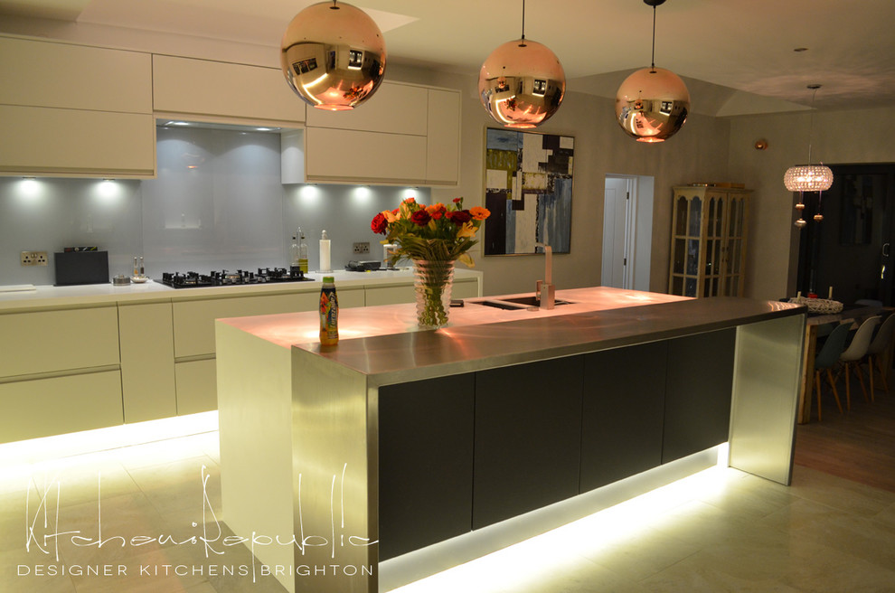 Photo of a large modern l-shaped eat-in kitchen in Sussex with an undermount sink, flat-panel cabinets, grey cabinets, stainless steel benchtops, blue splashback, glass sheet splashback, stainless steel appliances, porcelain floors and with island.