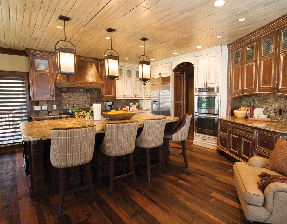 Example of a large mountain style l-shaped dark wood floor open concept kitchen design with recessed-panel cabinets, medium tone wood cabinets, stone slab backsplash, stainless steel appliances and an island