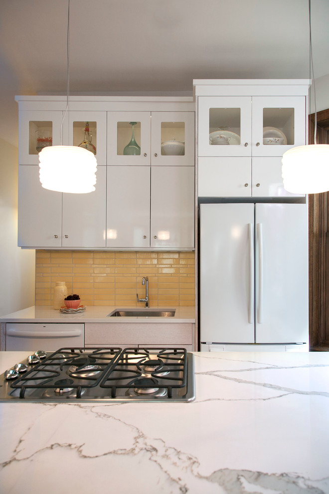 Inspiration for a mid-sized transitional l-shaped medium tone wood floor eat-in kitchen remodel in Chicago with an undermount sink, shaker cabinets, white cabinets, quartz countertops, yellow backsplash, ceramic backsplash, white appliances and an island
