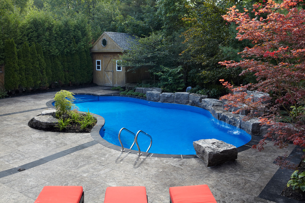 Large contemporary backyard custom-shaped natural pool in Toronto with a water feature and stamped concrete.