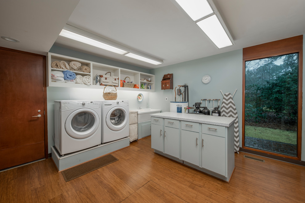 Inspiration for a large midcentury dedicated laundry room in Other with blue walls, a side-by-side washer and dryer, a double-bowl sink, open cabinets, white cabinets, grey benchtop and cork floors.