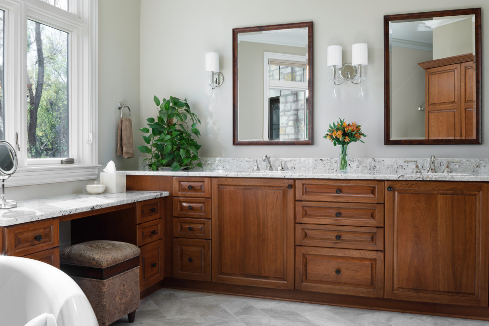 Large traditional master bathroom in Milwaukee with raised-panel cabinets, medium wood cabinets, a freestanding tub, a double shower, a one-piece toilet, beige walls, marble floors, an undermount sink, granite benchtops, beige floor, a hinged shower door, white benchtops, an enclosed toilet, a double vanity and a built-in vanity.