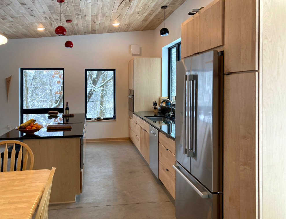 Foto på ett stort funkis svart kök och matrum, med släta luckor, skåp i ljust trä, granitbänkskiva, svart stänkskydd, rostfria vitvaror, betonggolv, en köksö och grått golv