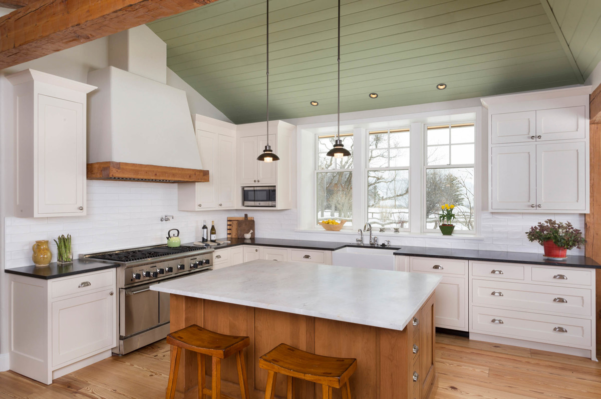 Large country l-shaped eat-in kitchen in Denver with a farmhouse sink, shaker cabinets, white cabinets, white splashback, with island, quartz benchtops, subway tile splashback, panelled appliances, medium hardwood floors, brown floor and black benchtop.