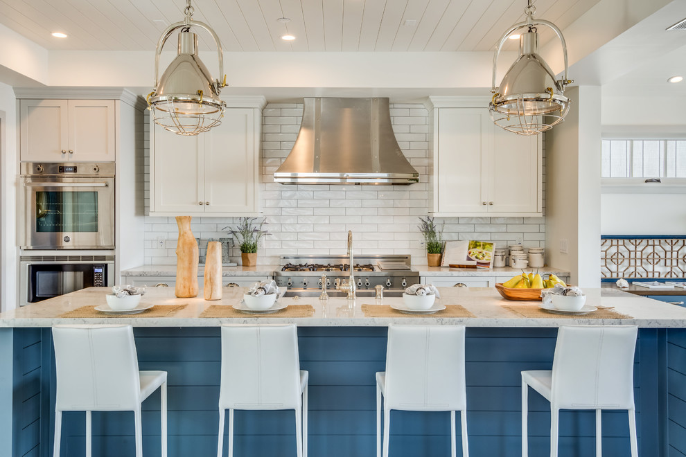 Beach style kitchen in Los Angeles with shaker cabinets, white cabinets, white splashback, subway tile splashback, stainless steel appliances and with island.