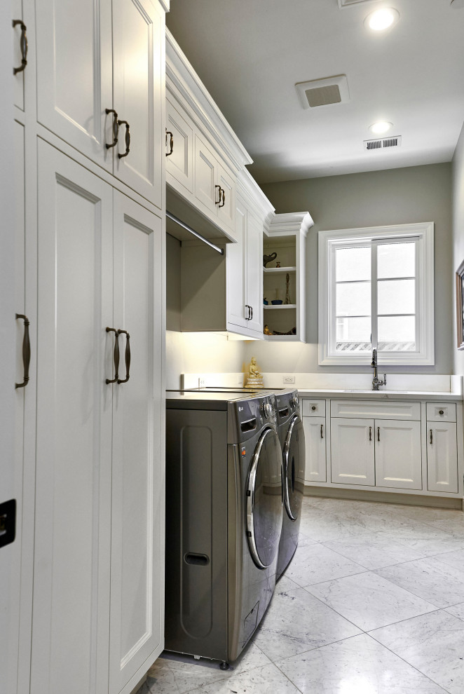 This is an example of a large traditional u-shaped utility room in San Francisco with a drop-in sink, flat-panel cabinets, white cabinets, quartz benchtops, white splashback, engineered quartz splashback, grey walls, marble floors, a side-by-side washer and dryer, grey floor and white benchtop.
