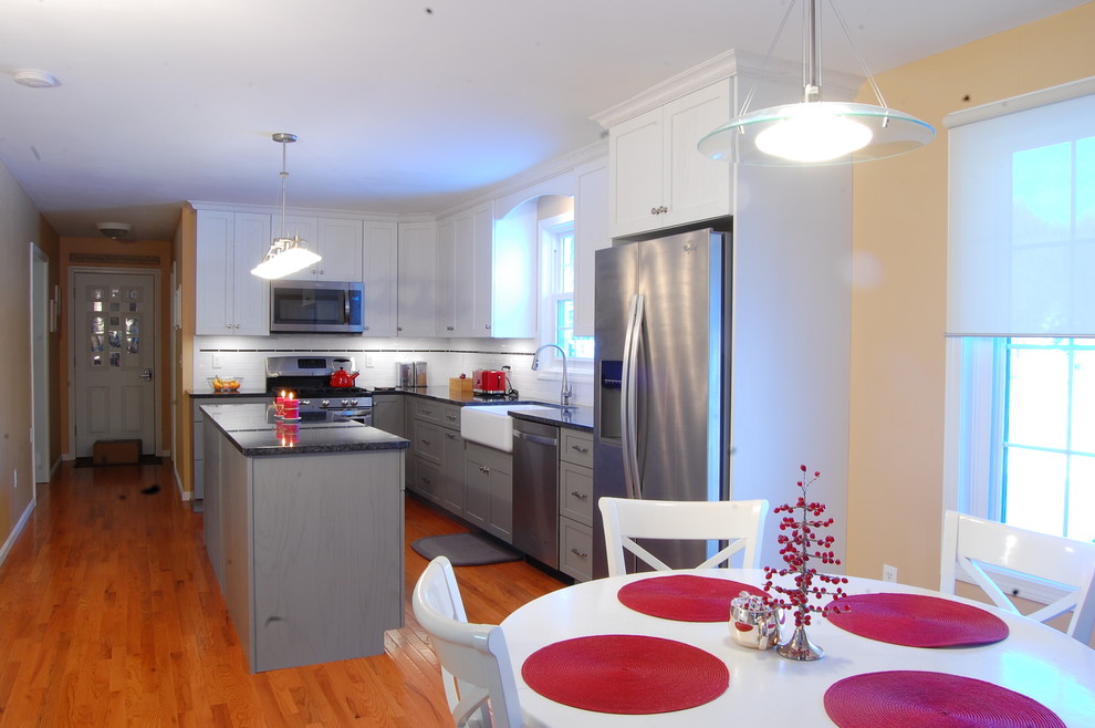 Mid-sized transitional l-shaped medium tone wood floor eat-in kitchen photo in Boston with a farmhouse sink, shaker cabinets, white cabinets, quartz countertops, white backsplash, subway tile backsplash, stainless steel appliances and an island