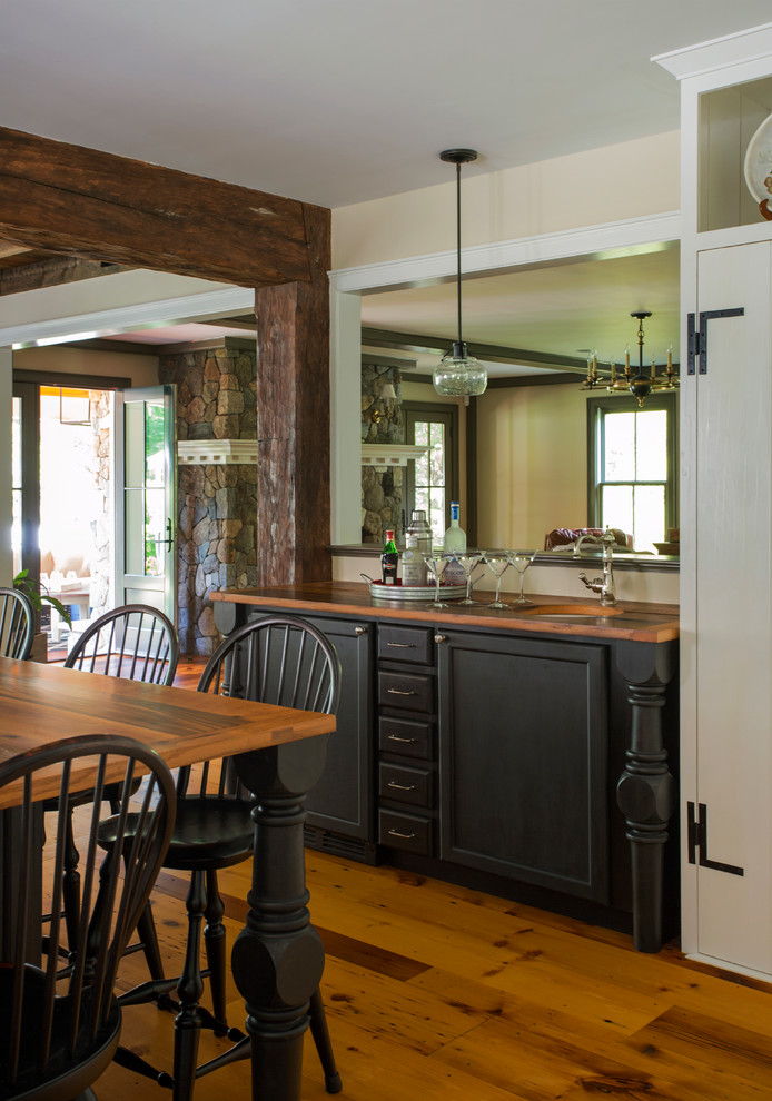 This is an example of a mid-sized country u-shaped eat-in kitchen in Boston with a farmhouse sink, white cabinets, stainless steel appliances, light hardwood floors, with island, flat-panel cabinets, white splashback, mirror splashback and wood benchtops.