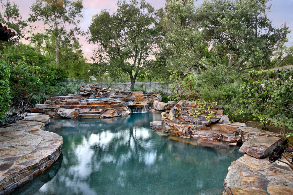 Large country backyard custom-shaped natural pool in Orange County with natural stone pavers.