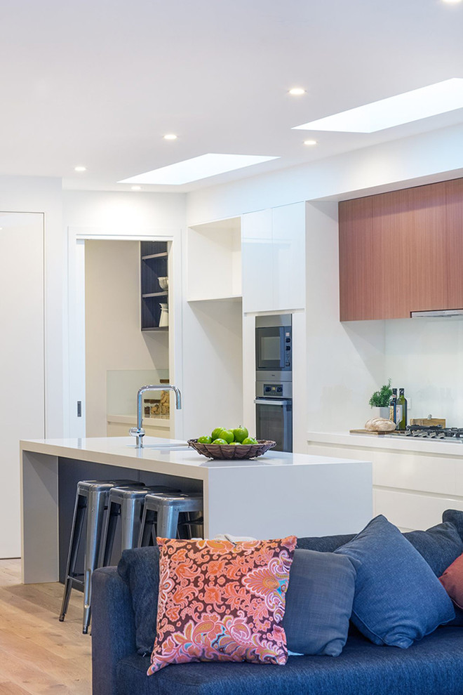 Inspiration for a mid-sized contemporary galley open plan kitchen in Melbourne with a double-bowl sink, medium wood cabinets, white splashback, stainless steel appliances, light hardwood floors and with island.