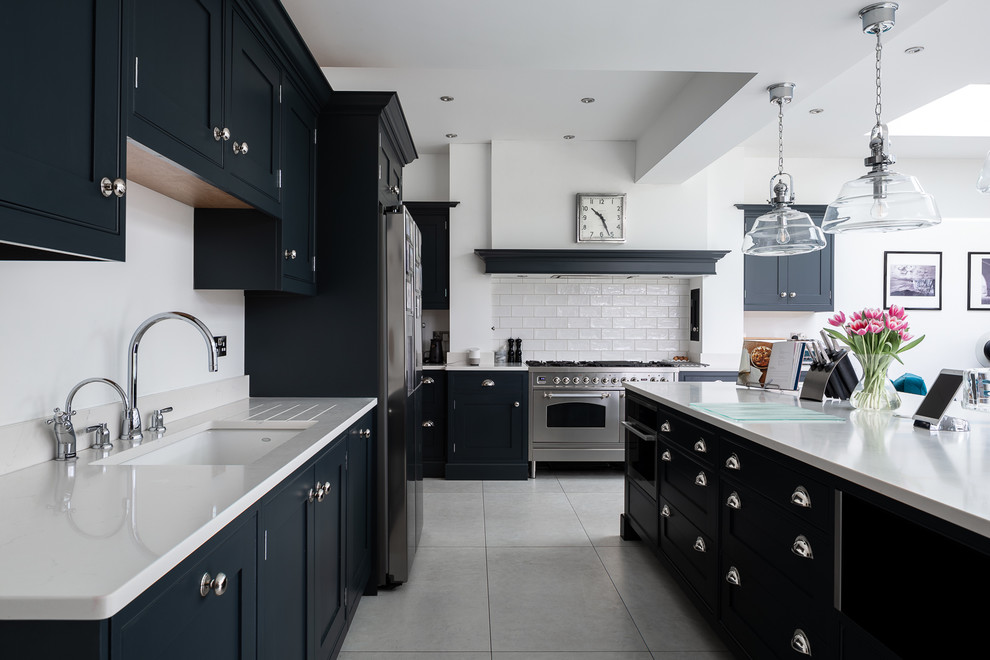 Design ideas for a transitional l-shaped kitchen in Hertfordshire with an undermount sink, beaded inset cabinets, black cabinets, white splashback, subway tile splashback, stainless steel appliances, with island, grey floor and white benchtop.