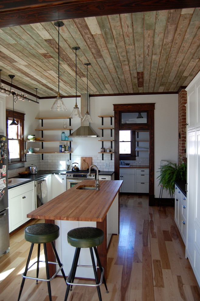 Mid-sized transitional l-shaped light wood floor enclosed kitchen photo with an undermount sink, shaker cabinets, white cabinets, soapstone countertops, white backsplash, subway tile backsplash and an island