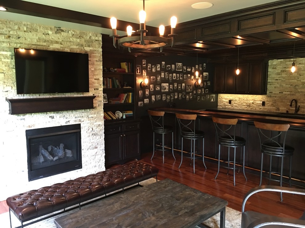 This is an example of a large country galley seated home bar in Other with dark hardwood floors, brown floor, an undermount sink, recessed-panel cabinets, dark wood cabinets, wood benchtops, beige splashback and stone tile splashback.