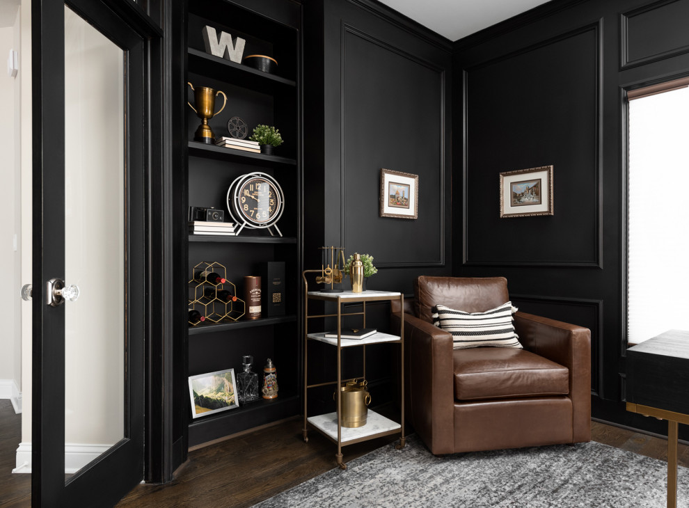 Imagen de despacho clásico renovado grande con paredes negras, suelo de madera oscura, chimenea de doble cara, marco de chimenea de piedra, escritorio independiente y boiserie