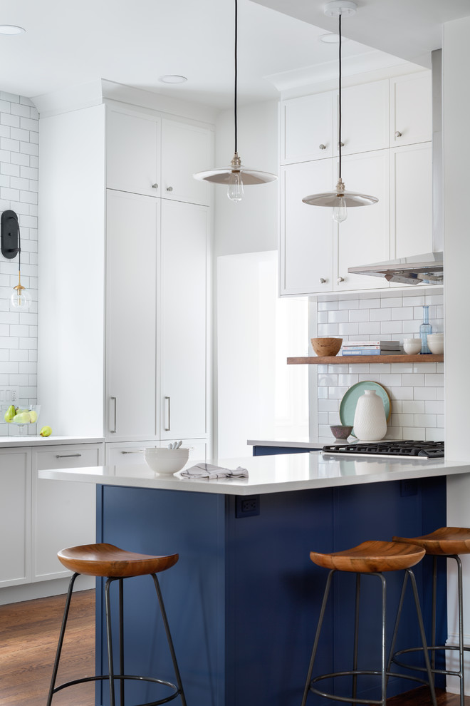 Example of a mid-sized transitional galley medium tone wood floor enclosed kitchen design with an undermount sink, shaker cabinets, beige cabinets, white backsplash, subway tile backsplash, stainless steel appliances, a peninsula and white countertops