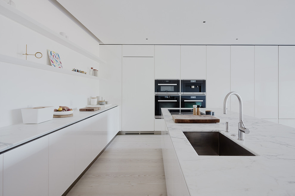 Contemporary eat-in kitchen in San Francisco with an undermount sink, flat-panel cabinets, white cabinets, marble benchtops, white splashback, light hardwood floors and with island.