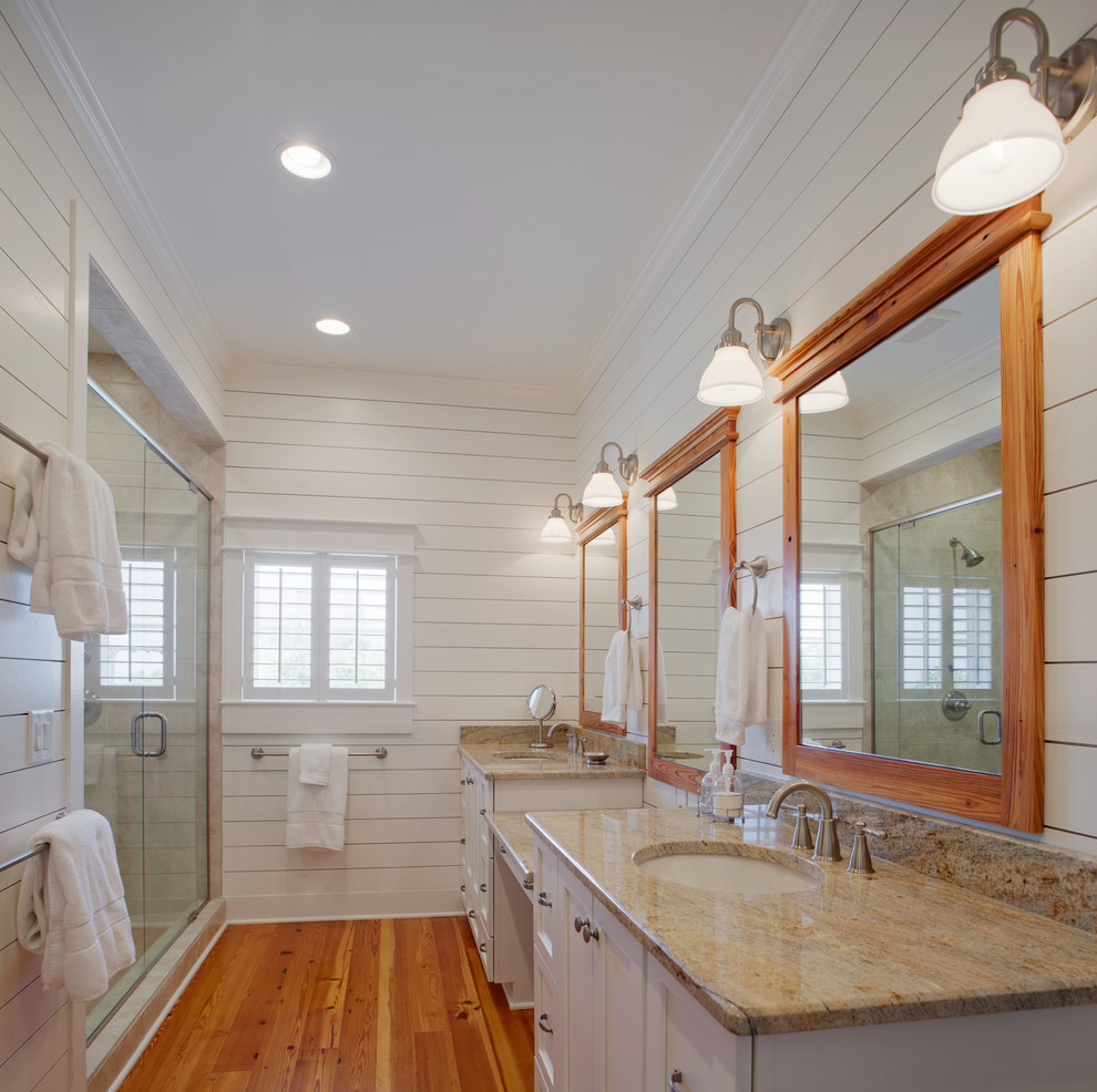 Large beach style master bathroom in Charleston with an undermount sink, louvered cabinets, white cabinets, granite benchtops, a corner shower, a one-piece toilet, white walls, medium hardwood floors, white tile and subway tile.