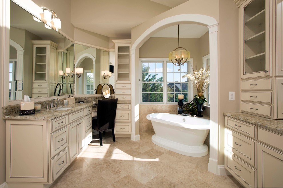 Inspiration for a large traditional master bathroom in DC Metro with recessed-panel cabinets, beige cabinets, beige tile, granite benchtops, a freestanding tub, a two-piece toilet, travertine, beige walls, travertine floors, an undermount sink and beige floor.