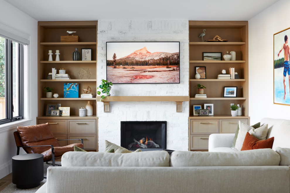 Cette photo montre un salon tendance de taille moyenne et fermé avec un mur blanc, une cheminée standard, un manteau de cheminée en brique, un téléviseur fixé au mur, un sol en bois brun et un sol marron.