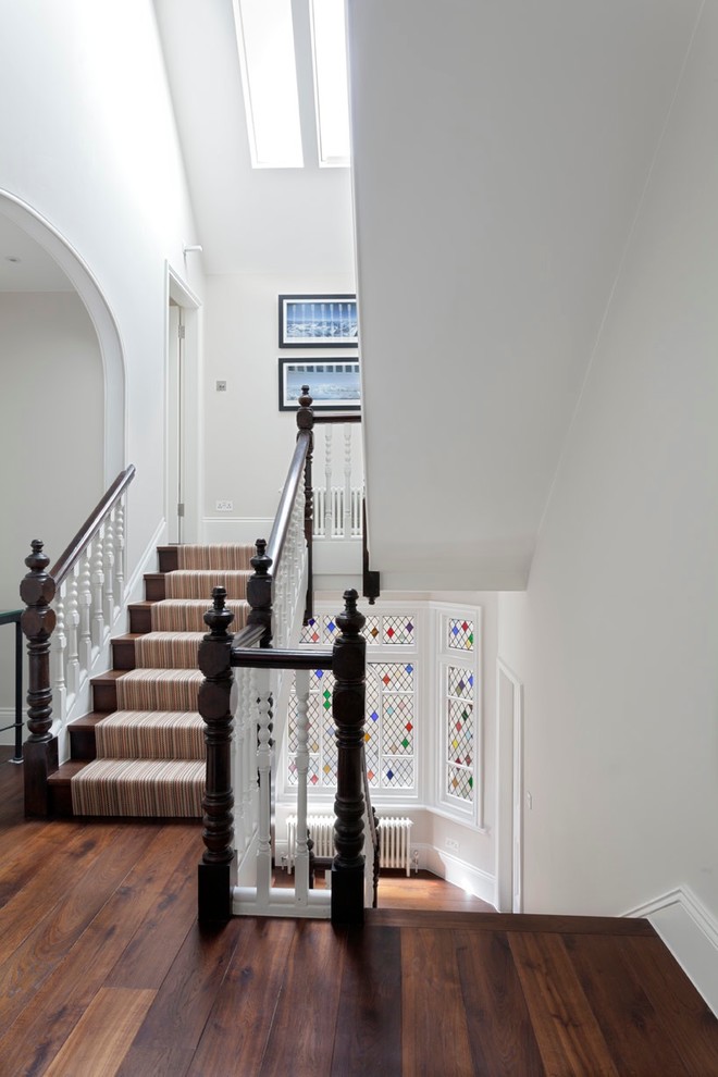 Photo of a large traditional carpeted u-shaped staircase in London with carpet risers and wood railing.