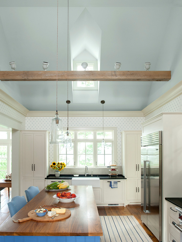 Beach style l-shaped kitchen in Portland Maine with a farmhouse sink, shaker cabinets, white cabinets, grey splashback, stainless steel appliances, medium hardwood floors and with island.