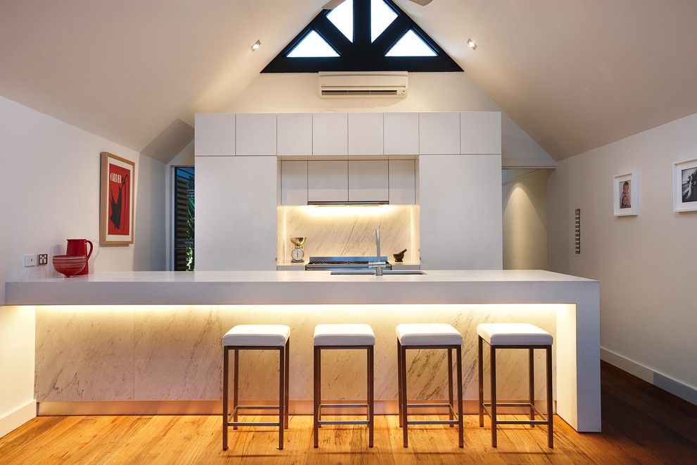 Inspiration for a contemporary kitchen in Melbourne with flat-panel cabinets, white cabinets, white splashback, stone slab splashback, medium hardwood floors and a peninsula.