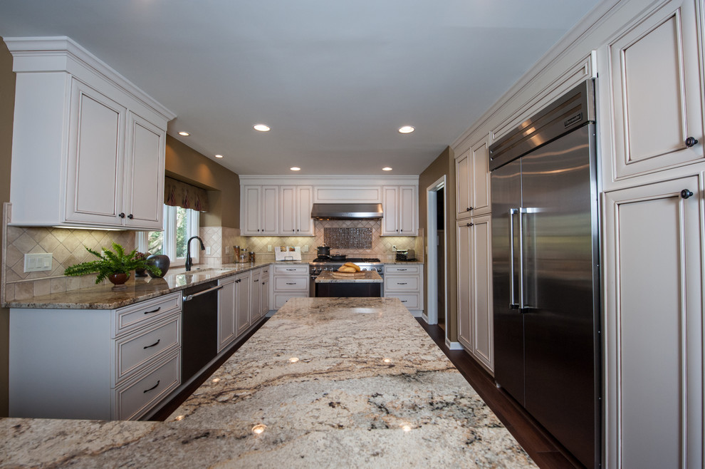 Inspiration for a large traditional l-shaped eat-in kitchen in Detroit with an undermount sink, recessed-panel cabinets, white cabinets, granite benchtops, brown splashback, stone tile splashback, stainless steel appliances, dark hardwood floors and multiple islands.