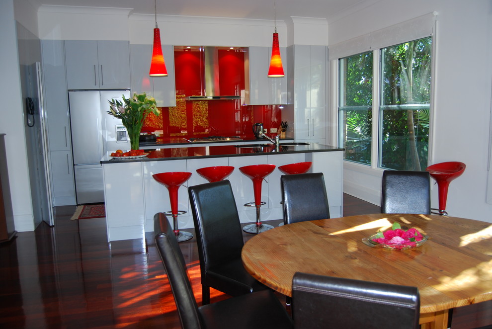 Photo of a mid-sized contemporary l-shaped eat-in kitchen in Sydney with an undermount sink, flat-panel cabinets, white cabinets, red splashback, glass sheet splashback, stainless steel appliances, dark hardwood floors and with island.