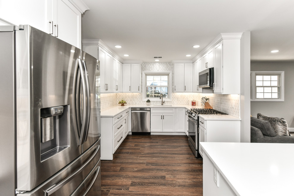 Mid-sized modern u-shaped kitchen in DC Metro with an undermount sink, shaker cabinets, white cabinets, quartzite benchtops, white splashback, marble splashback, stainless steel appliances, vinyl floors, with island, brown floor and white benchtop.