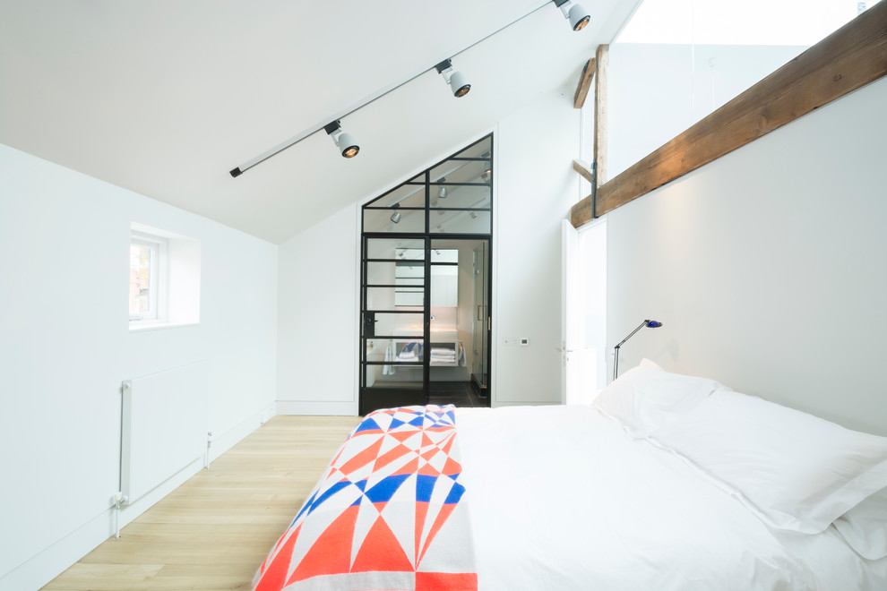 Design ideas for an expansive industrial loft-style bedroom in London with white walls and light hardwood floors.