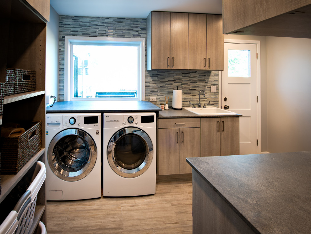 シカゴにあるコンテンポラリースタイルのおしゃれな家事室 (スロップシンク、フラットパネル扉のキャビネット、ヴィンテージ仕上げキャビネット、コンクリートカウンター、青いキッチンパネル、ガラスタイルのキッチンパネル、グレーの壁、セラミックタイルの床、左右配置の洗濯機・乾燥機、グレーの床、グレーのキッチンカウンター) の写真