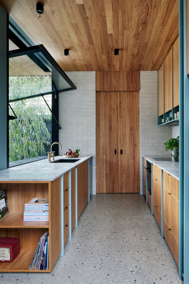 Photo of a small midcentury galley open plan kitchen in Melbourne with an undermount sink, recessed-panel cabinets, light wood cabinets, marble benchtops, grey splashback, marble splashback, black appliances, concrete floors, no island, grey floor, grey benchtop and wood.