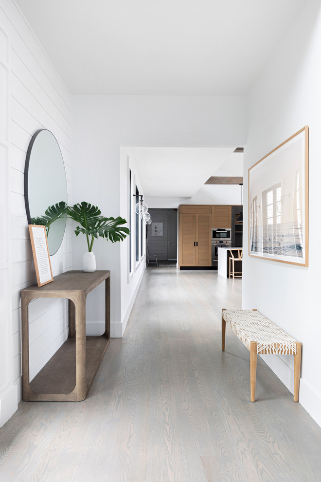 This is an example of a mid-sized beach style mudroom in New York with white walls, dark hardwood floors, a single front door, a white front door and grey floor.