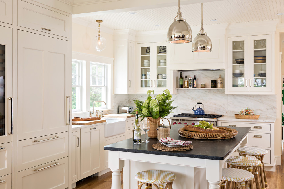 This is an example of a mid-sized transitional l-shaped open plan kitchen in Boston with a farmhouse sink, beaded inset cabinets, white cabinets, marble benchtops, white splashback, stone slab splashback, panelled appliances, medium hardwood floors and with island.