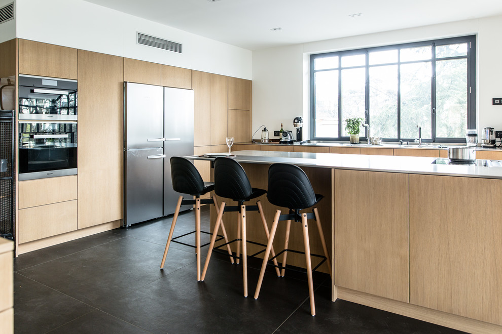 This is an example of a contemporary kitchen in Lyon with an integrated sink, beaded inset cabinets, light wood cabinets, stainless steel benchtops, stainless steel appliances, cement tiles and black floor.