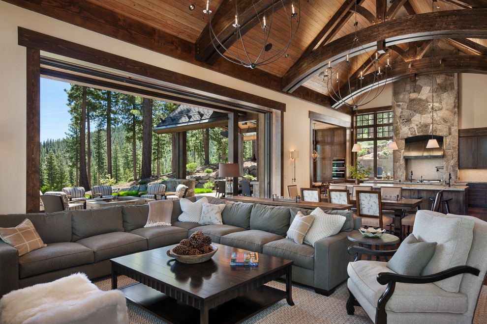 This is an example of a large open concept living room in Sacramento with beige walls, dark hardwood floors, a standard fireplace, a stone fireplace surround, a wall-mounted tv and brown floor.