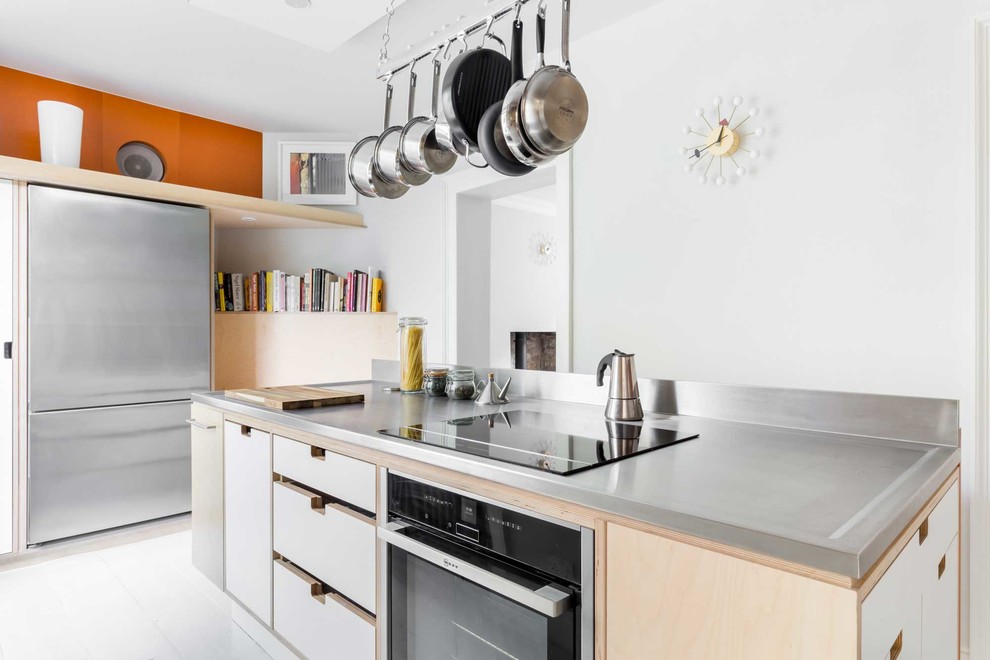 Photo of a mid-sized contemporary u-shaped separate kitchen in Other with flat-panel cabinets, white cabinets, stainless steel benchtops, stainless steel appliances, light hardwood floors, with island, white floor, a drop-in sink and orange splashback.